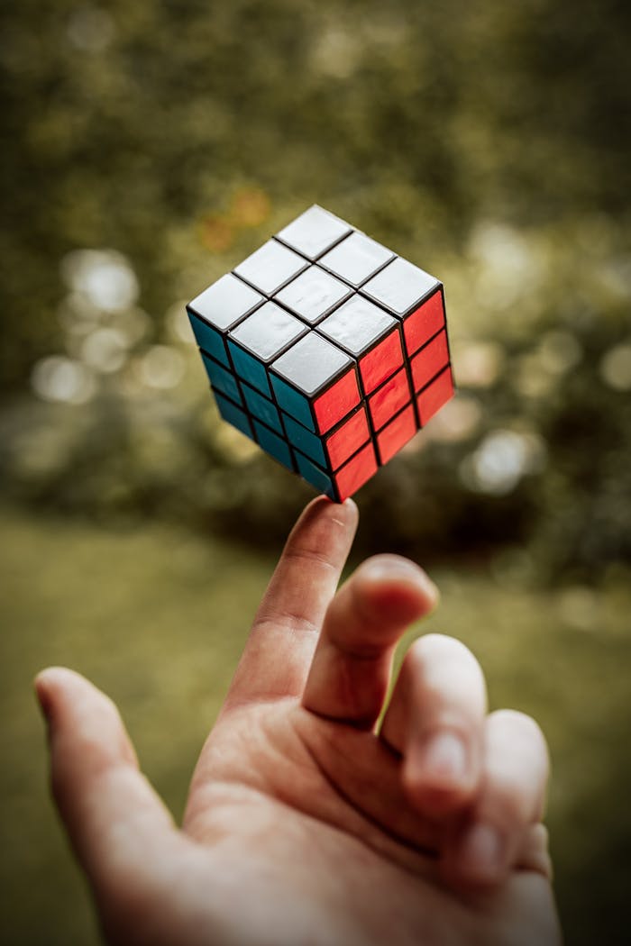 A Rubik's Cube balanced on a finger with a blurred outdoor background.